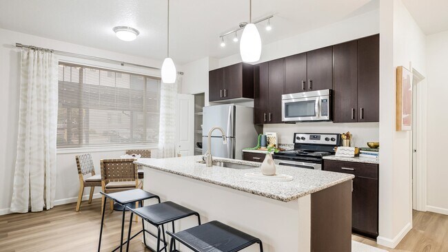 Modern kitchens feature granite countertops, stainless steel appliances, and spacious islands - Victory Flats at Elmonica Station Apartments