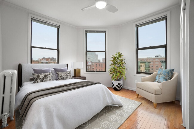 Bright and airy bedroom with three large windows, offering stunning city views, stylish decor, and a comfortable lounge chair.