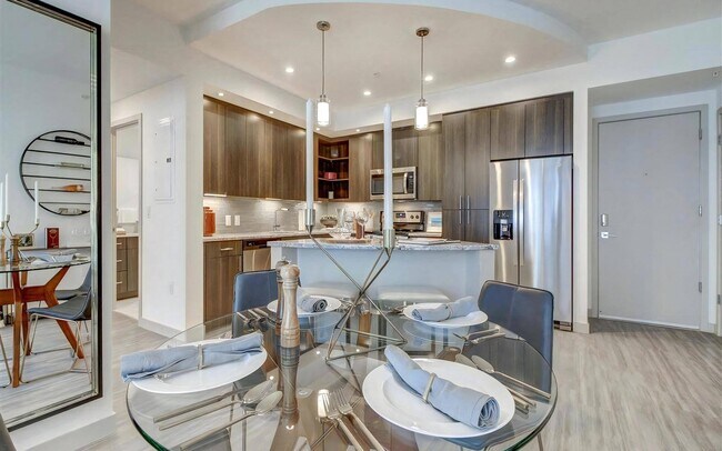 Comedor con mesa redonda de vidrio y vista abierta a la cocina de acero inoxidable - Pearl Flagler Village