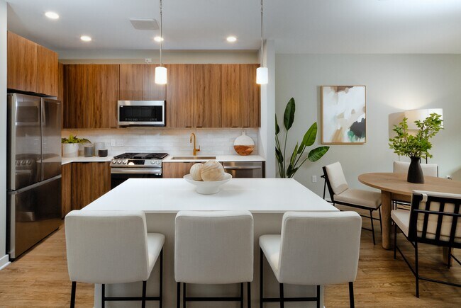 Upgraded Collection kitchen with stainless steel appliances, neutral quartz countertops, dark brown cabinetry, light grey backsplash, and hard surface flooring (model home)