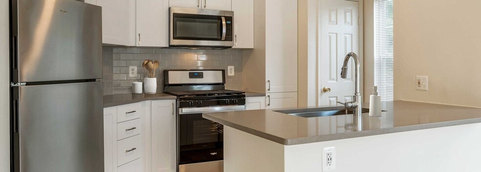 Renovated Package IV kitchens with white cabinetry, grey quartz countertops, stainless steel appliances, grey tile backsplash, and hard surface plank flooring