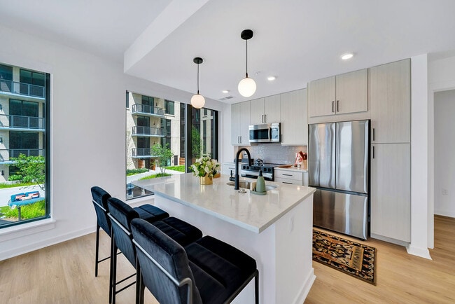 Kitchen with white island, stainless appliances, black barstools, pendant lights, and large windows and stainless steel appliances
