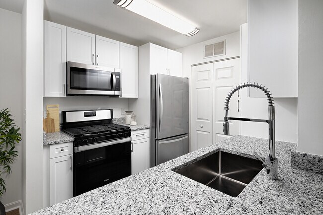 Phase I Renovated apartment kitchen with stainless steel appliances, grey speckled granite countertop, and white cabinetry