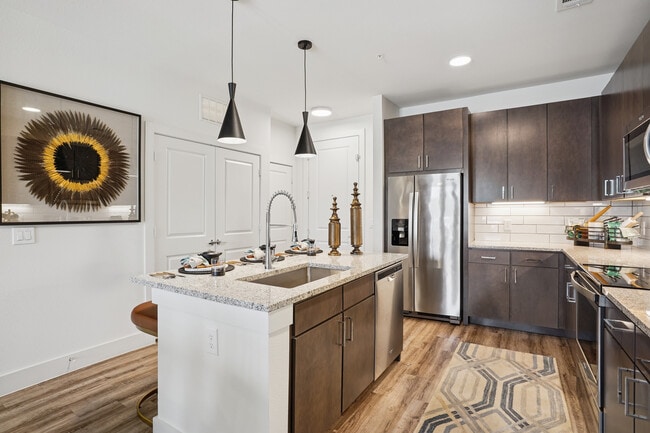 Kitchen with espresso cabinetry, speckled granite countertops, white tile backsplash, stainless steel appliances, and hard surface flooring