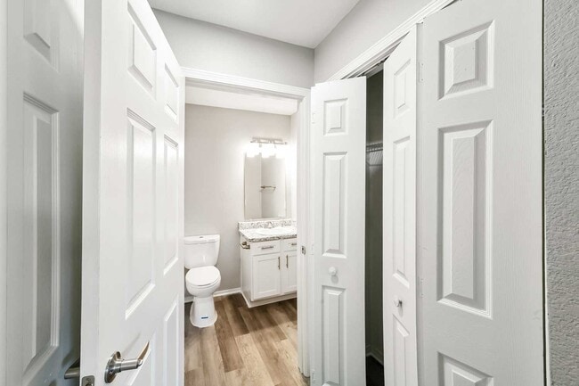 Hallway view with multiple doors leading to bathroom, closet, and bedroom spaces with wood style flooring and neutral walls