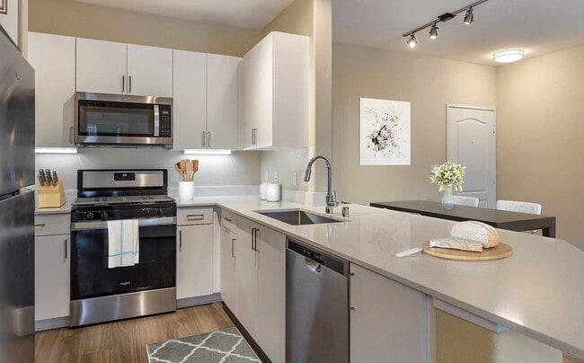 Renovated Package I kitchens with light grey quartz countertops, new white cabinetry, stainless steel appliances, upgraded fixtures, and hard surface flooring throughout