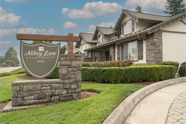 Charming entrance to Abbey Lane Apartments surrounded by manicured gardens and elegant stone features, under a picturesque sky. - Abbey Lane Apartments