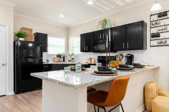 Cocine con estilo con electrodomésticos negros y una barra de desayuno en Seaglass Apartments: actualice su hogar en Corpus Christi - Seaglass Apartments & Townhomes