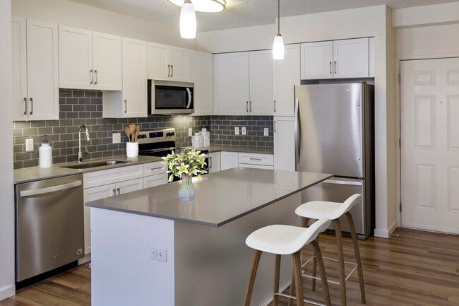 Renovated Package II kitchen with grey quartz countertops, white shaker cabinetry, stainless steel appliances, grey tile backsplash, and hard surface flooring throughout