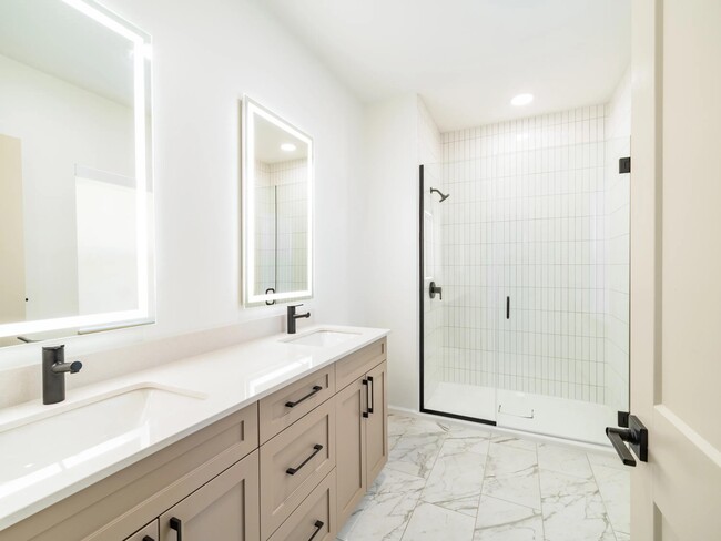 Primary bathroom with a double-sink vanity, illuminated mirrors, and a glass-enclosed shower finished with clean lines and timeless materials.