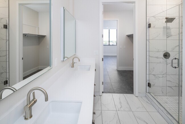 Signature Collection bathroom with grey cabinetry, white quartz countertop, lighted vanity mirrors, porcelain shower surround, and porcelain tile flooring - Avalon South Miami