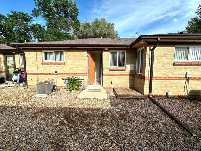 Charming brick exterior of a cozy home with a welcoming open door, surrounded by a low-maintenance rock garden and lush greenery. - Flats at 16th