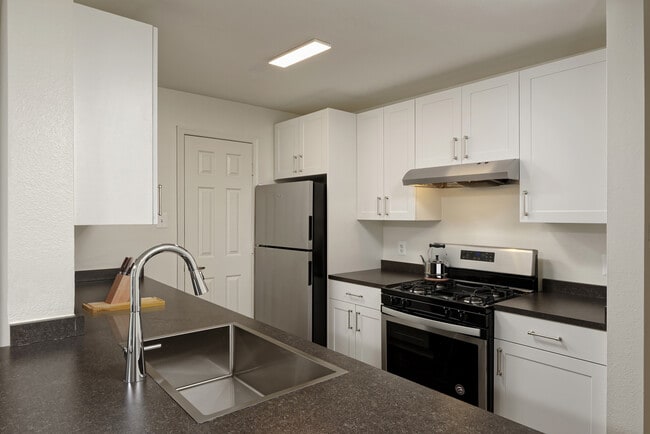 Renovated Package II kitchen with white cabinetry, dark grey laminate countertops, stainless steel appliances, and hard surface flooring