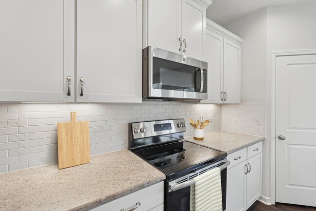 Upgrade Package kitchen with white cabinetry, designer tile backsplash, granite countertops, and stainless steel appliances