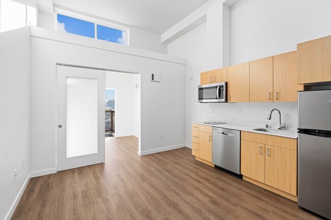 Enjoy cooking in this modern kitchen featuring sleek wood flooring, ample cabinet space, and a clean, open design. - Harbor Flats
