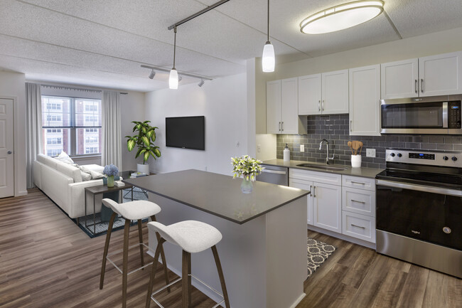 Renovated Package II kitchen with grey quartz countertops, white shaker cabinetry, stainless steel appliances, grey tile backsplash, and hard surface flooring throughout - Avalon Natick Apartments