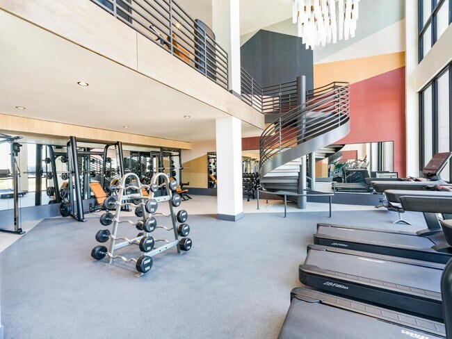Expansive two-story fitness center with free weights, cardio equipment, and a sculptural staircase connecting dedicated spaces for training and recovery.