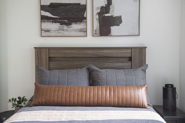 Dormitorio contemporáneo con una elegante cabecera de madera, acogedoras almohadas grises y marrones y arte de pared abstracto moderno.
