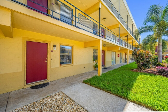 Charming apartment exterior featuring bright yellow walls, red doors, and vibrant landscaping with palm trees. - Parkview Apartments