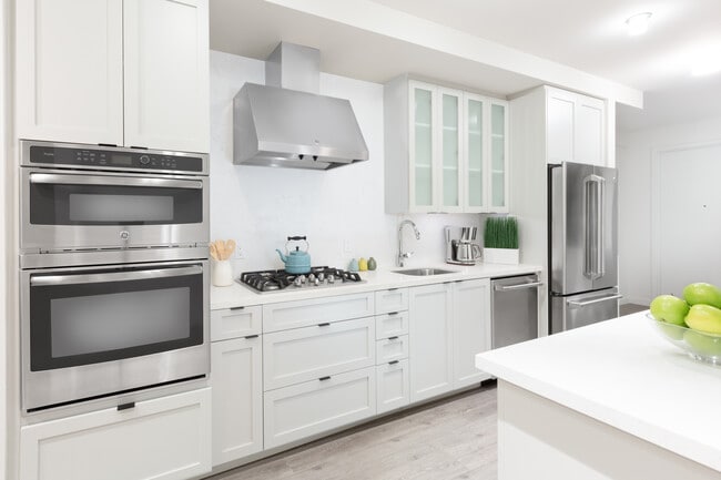 Kitchen with white cabinetry, quartz stone countertops, ceramic tile backsplash and stainless steel appliances - Avalon Dogpatch Apartments