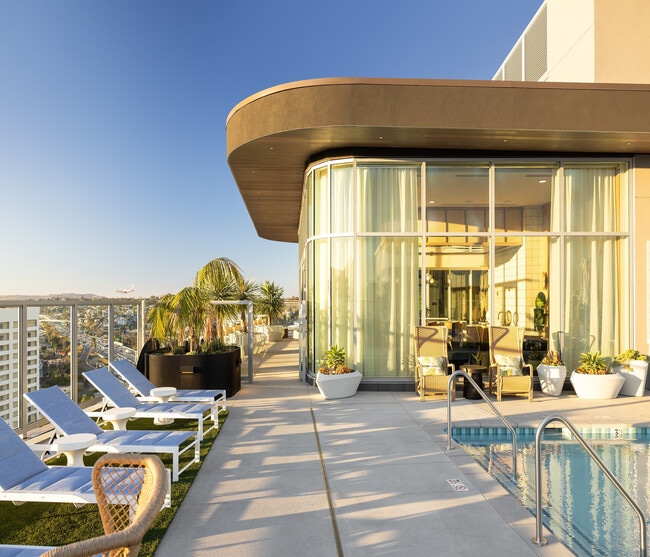 Luxurious rooftop pool area with sleek lounge chairs, panoramic city views, and modern glass-encased lounge in a vibrant high-rise setting.
