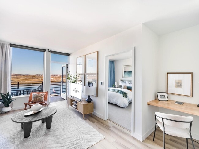 Bright, open living with a dedicated workspace and balcony views just beyond.