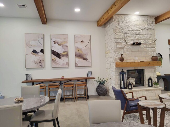 Stone fireplace beside round dining tables and abstract wall art, with high ceilings and wood beams overhead