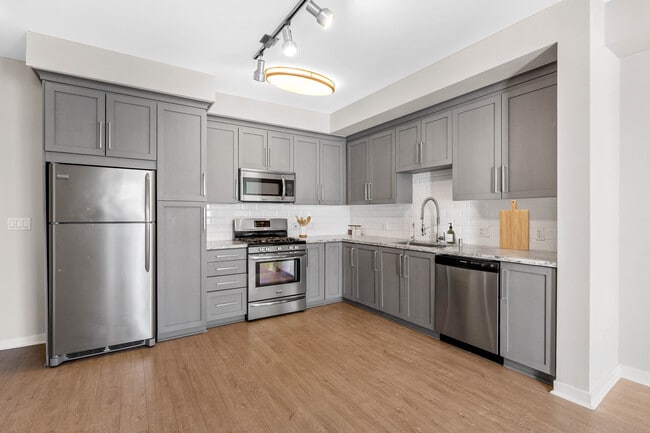 Kitchens with grey cabinetry, grey speckled granite countertops, white subway tile backsplash, stainless steel appliances, and hard surface flooring