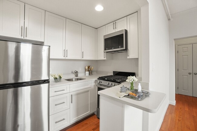 Cocina moderna con elegantes electrodomésticos de acero inoxidable, armarios blancos de diseño y cálidos suelos de madera noble, perfecta para los amantes de la cocina. - Atrio Boston