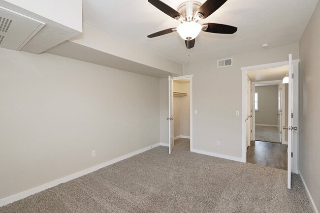 Bedroom with carpet flooring, ceiling fan, open closet, and doorway leading to hallway with wood style flooring