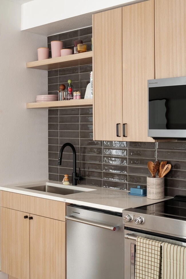 Streamlined cabinetry, open shelving, and a glossy tile backsplash bring warmth and texture to this thoughtfully designed kitchen.