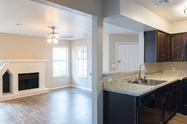 Open floor plan with dark wood kitchen cabinets, granite countertops, wood-look floors, and white brick fireplace