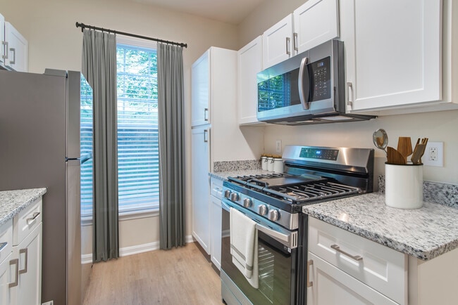 Renovated Package II kitchen with stainless steel appliances, white speckled quartz countertops, white cabinetry, and hard surface flooring - Avalon at Traville