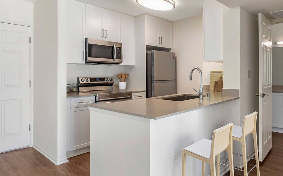 Renovated Package I kitchen with stainless steel appliances, beige quartz countertops, new white cabinetry, and hard surface flooring