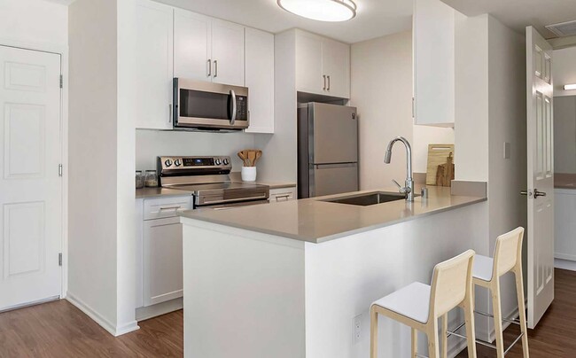 Renovated Package I kitchen with stainless steel appliances, beige quartz countertops, new white cabinetry, and hard surface flooring - eaves Woodland Hills Apartments