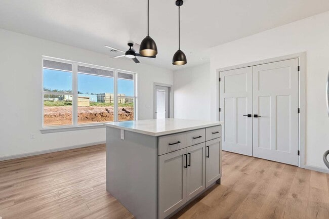 Kitchen with central island, pendant lighting, stainless steel appliances, and hallway with recessed lighting