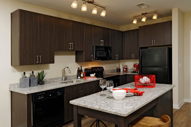 Contemporary kitchen with espresso cabinetry, grey speckled granite countertops, black appliances, and hard surface flooring