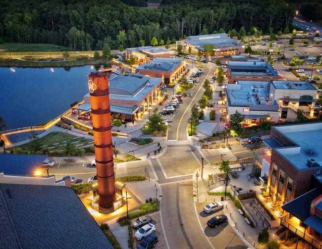 Aerial view of a vibrant shopping center by the lake at dusk, featuring well-lit pathways and modern architecture.