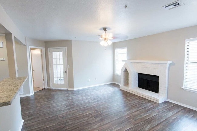 Vacant living room with white brick fireplace, dark wood-look floors, ceiling fan, and French door leading outside