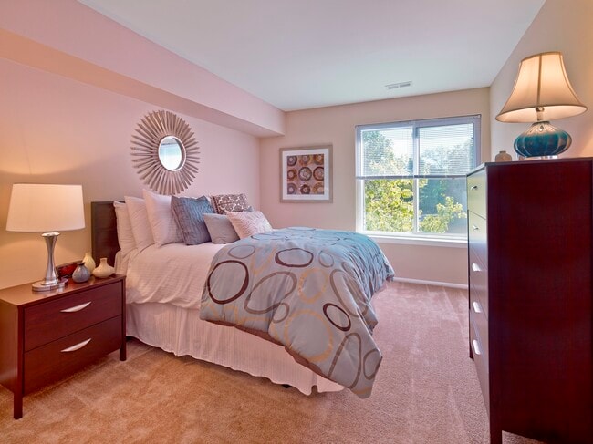 This cozy bedroom at Haynes Run Apartments features soft carpeting, modern furnishings, and a large window that fills the room with sunlight and scenic views.