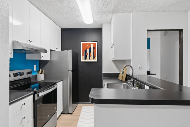 Renovated Package I kitchen with updated stainless steel appliances, white cabinetry, black laminate countertops, and updated hard surface flooring