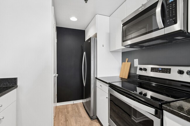 Cocina renovada del Paquete I con gabinetes blancos, encimeras de granito negro, electrodomésticos de acero inoxidable y pisos de superficie dura.