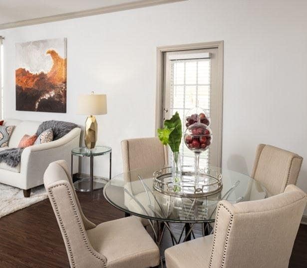 Una mesa de comedor de cristal rodeada de sillas y un jarrón con flores encima. - Glenhaven at Star Ranch