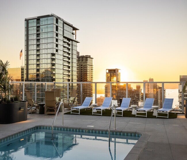 Luxurious rooftop pool with sun loungers and breathtaking skyline views at sunset, perfect for relaxation.