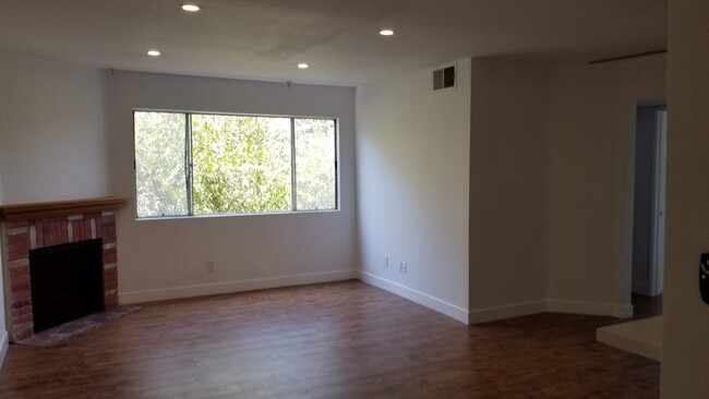 Living Room with wood panel floors, gas fireplace, LED lighting and red pipebrush tree in window. - 14126 Tiara St Townhome