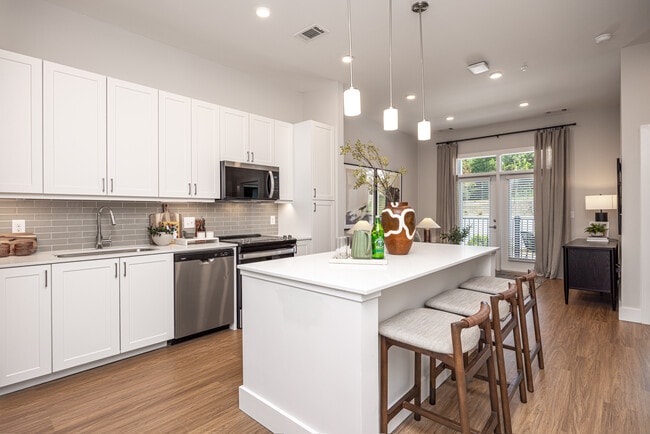 Modern kitchen with white cabinetry, undercabinet lighting, grey tile backsplash, and white quartz countertops - Avalon Carmel Commons