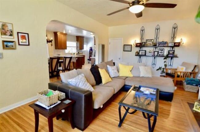 Living Room with original hardwood facing into open kitchen. room has ac unit, large overhead fan and large rounded window facing the street. - 4770 Bancroft St