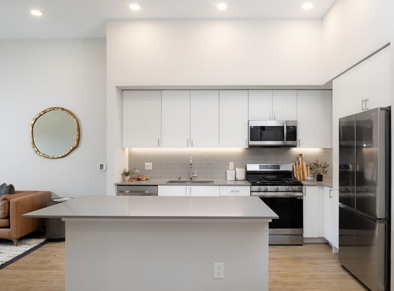 Kitchen with grey quartz countertops, white cabinetry, grey subway tile backsplash, stainless steel appliances, and hard surface flooring