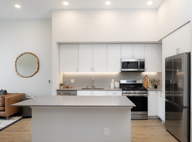 Kitchen with grey quartz countertops, white cabinetry, grey subway tile backsplash, stainless steel appliances, and hard surface flooring - Avalon Bothell Commons Rental
