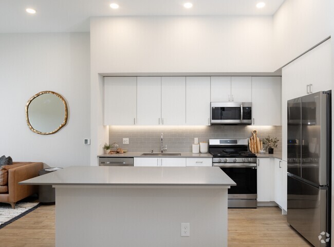 Kitchen with grey quartz countertops, white cabinetry, grey subway tile backsplash, stainless steel appliances, and hard surface flooring - Avalon Bothell Commons Rental